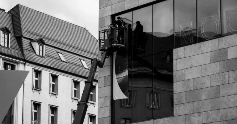 Pracownicy na podnośniku osadzają dużą taflę szkła na elewacji budynku