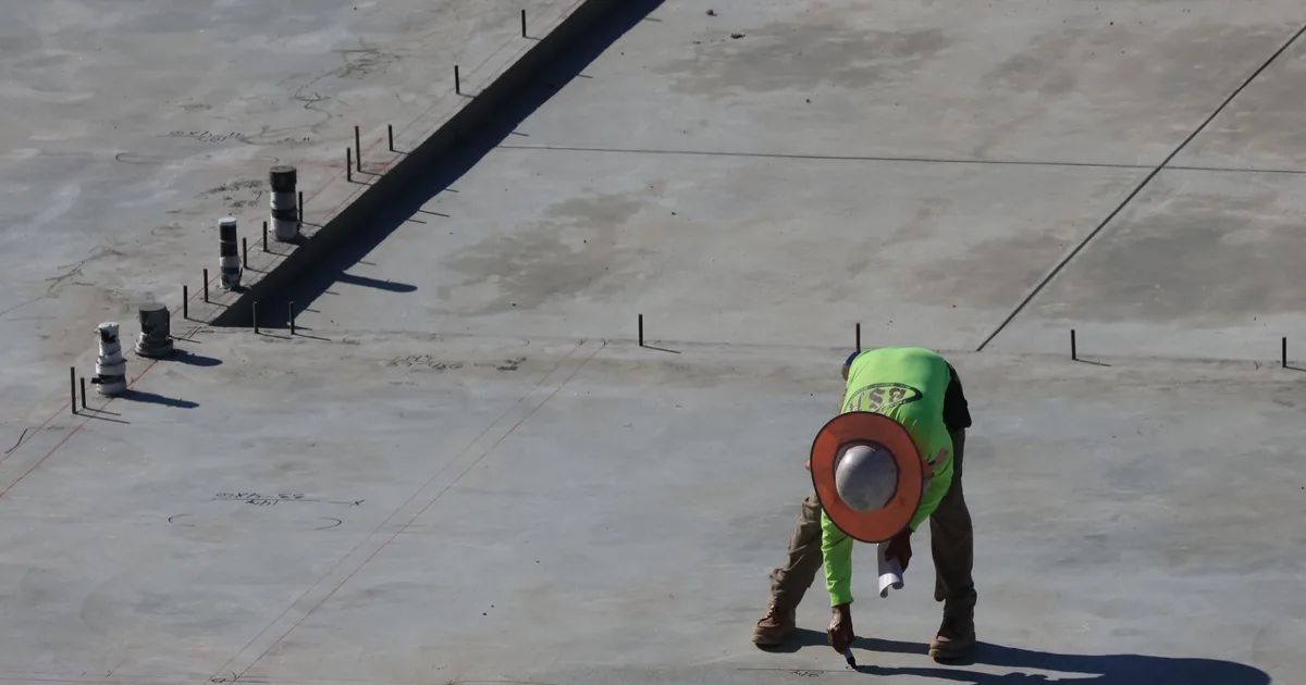 Robotnik pochylony nad betonową płytą na budowie w ostrym słońcu