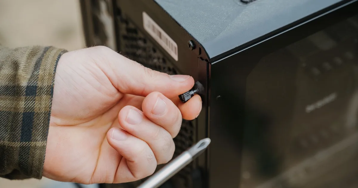 Dłoń odkręca wkrętakiem wkręt w metalowej obudowie urządzenia
