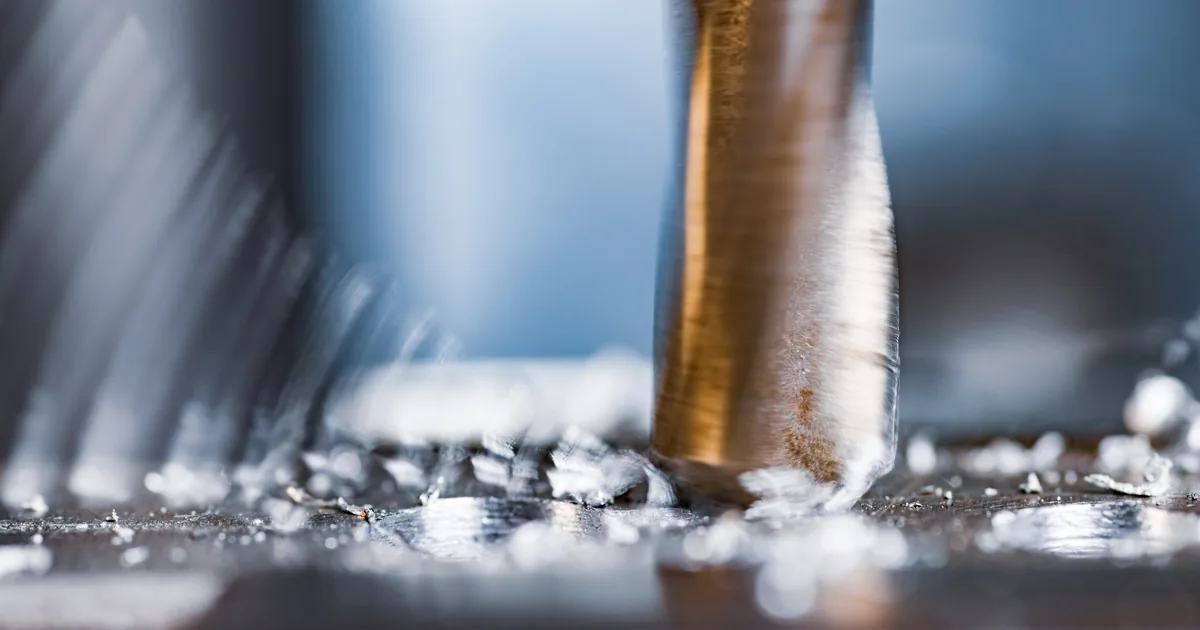 Zbliżenie na wiercenie w metalu, spod narzędzia schodzą zwijające się wióry
