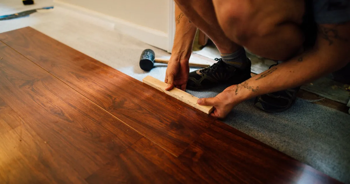 Fachowiec dobija gumowym młotkiem panel laminowany podczas układania podłogi