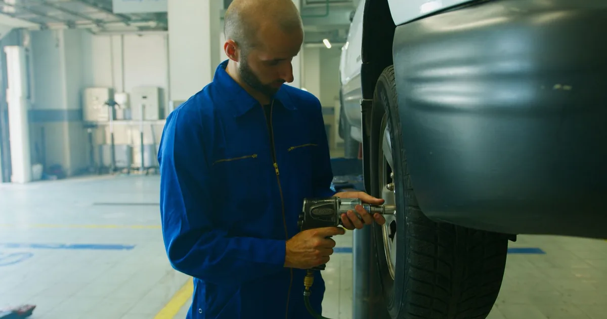 Mechanik w niebieskim kombinezonie odkręca koło kluczem udarowym w warsztacie