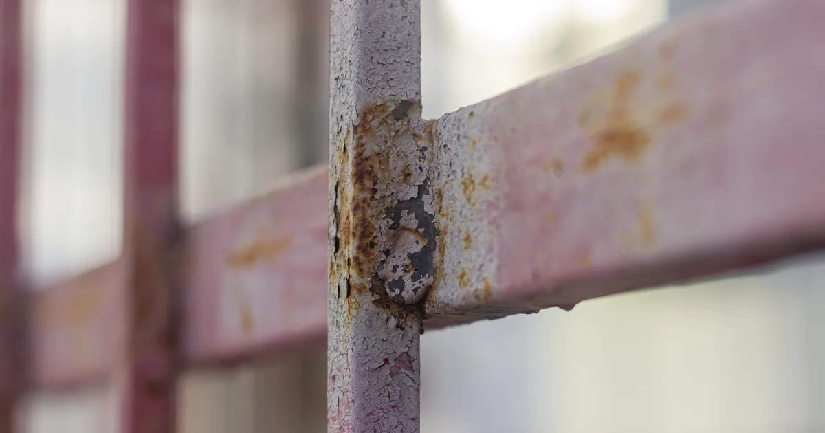 Rude wykwity rdzy przebijające przez różową farbę na metalowym ogrodzeniu