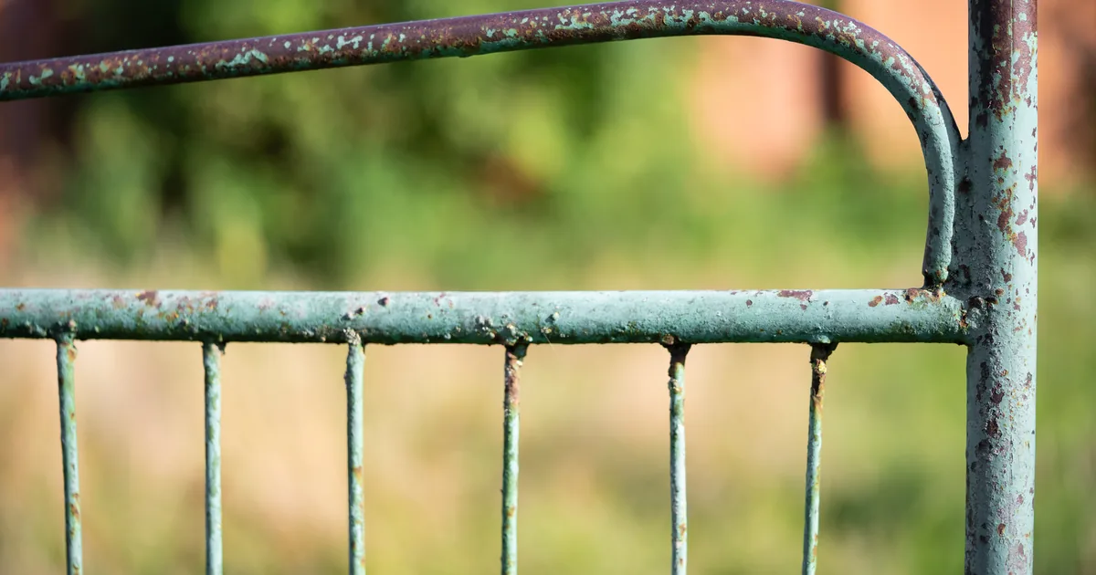 Stara metalowa brama z popękaną powłoką malarską i wychodzącą spod niej rdzą