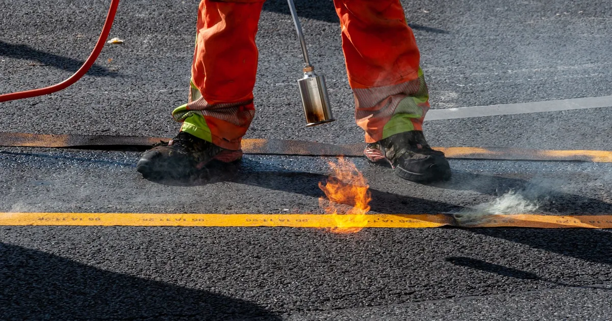 Pracownik zgrzewa palnikiem bitumiczną warstwę nawierzchni, praca przy otwartym ogniu