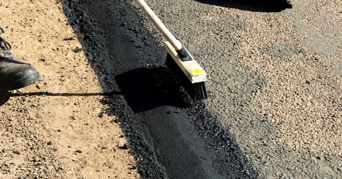 Naprawa nawierzchni asfaltowej, ciemna masa bitumiczna i narzędzia drogowca