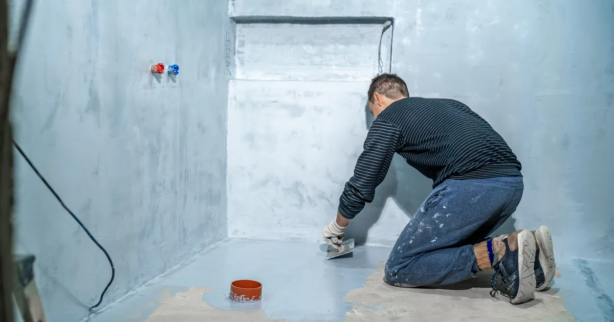 Fachowiec nakłada folię w płynie na posadzkę i ściany łazienki w stanie surowym przed klejeniem płytek