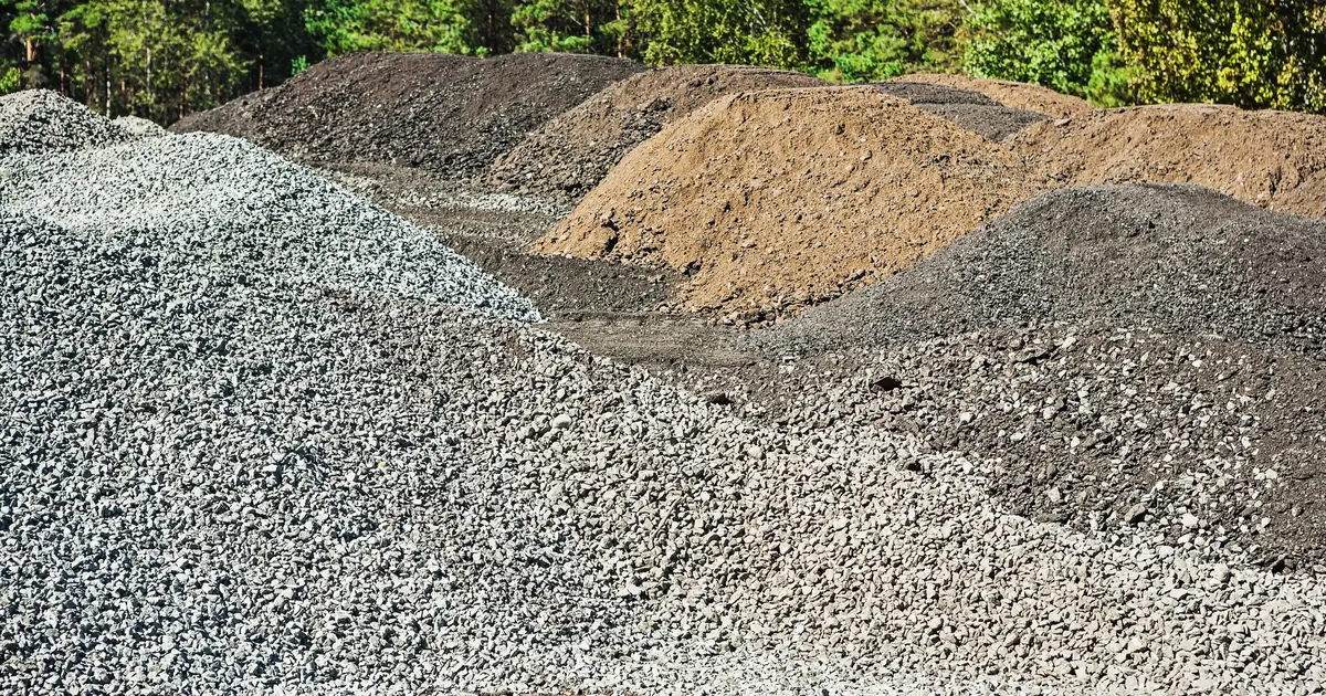 Pryzmy kruszywa, tłucznia i ziemi na placu budowy - materiały do utwardzania terenu pod dojazd